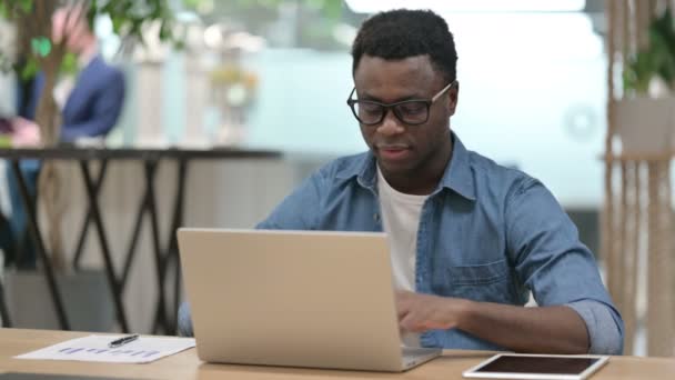 若いアフリカ人男性はノートパソコンで作業中にカメラで微笑む — ストック動画