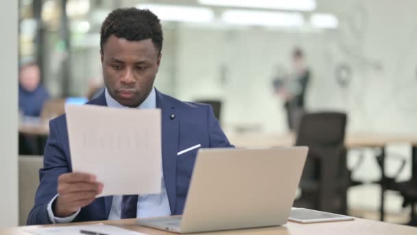 Afrikaanse zakenman het lezen van documenten tijdens het werken op laptop — Stockvideo