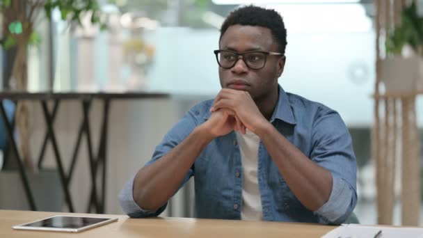 Ung afrikansk man sitter i moderna kontoret och tänker — Stockvideo