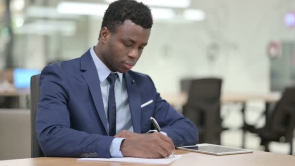 Εργατικός αφρικανός επιχειρηματίας που γράφει σε χαρτί στο γραφείο — Αρχείο Βίντεο