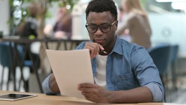 Joven africano leyendo documentos en la oficina moderna — Vídeos de Stock