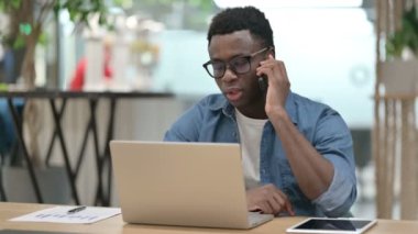 Laptop kullanırken Smartphone 'da konuşan kızgın Afrikalı adam 