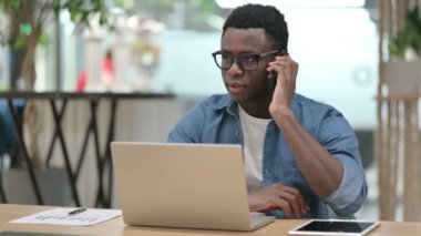 Laptop kullanırken akıllı telefondan konuşan genç Afrikalı adam. 