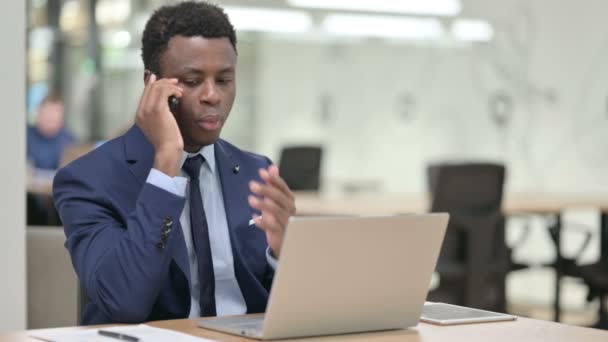 Dühös afrikai üzletember beszél Smartphone használata közben Laptop — Stock videók