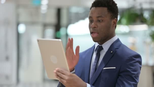 Appel vidéo sur tablette par un homme d'affaires africain dans un bureau moderne — Video