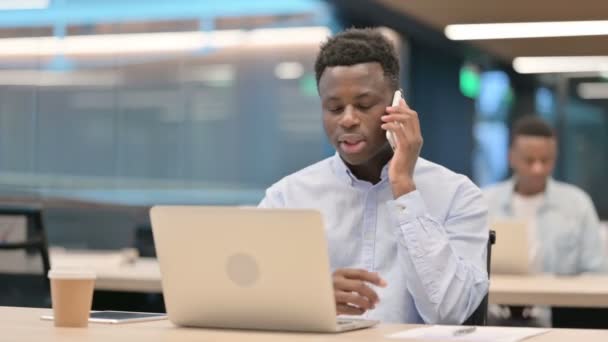 Dühös afrikai üzletember laptoppal beszél okostelefonon — Stock videók