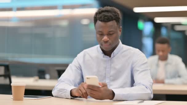 African Businessman Reacting to Loss on Smartphone in Office — Stock Video