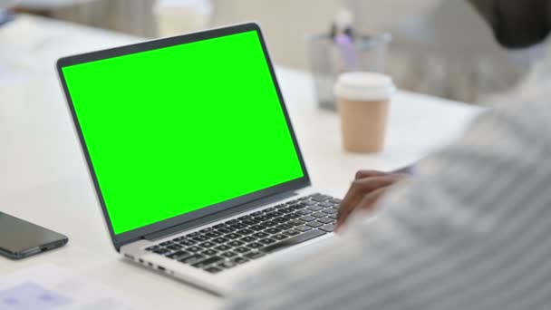 Vista trasera del hombre africano usando el ordenador portátil con la pantalla dominante verde del croma — Vídeo de stock