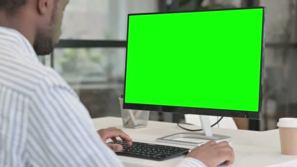 Vista trasera del hombre africano usando el escritorio con la pantalla verde de la llave del croma — Vídeo de stock