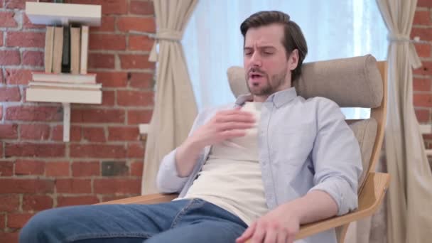 Joven tosiendo sentado en un sofá — Vídeos de Stock