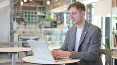 Cafe 'de dizüstü bilgisayar kullanırken kameraya bakan çekici genç adam.