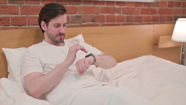 Jungunternehmer mit Smartwatch im Bett — Stockvideo