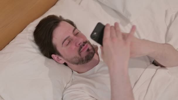 Casual νεαρός μιλώντας στο Smartphone, ενώ κοιμάται στο κρεβάτι — Αρχείο Βίντεο