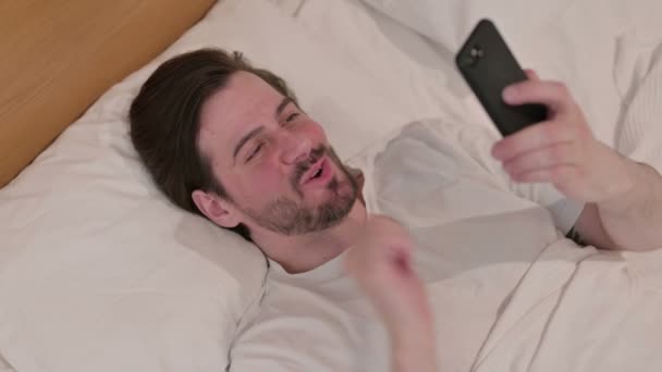カジュアル若い男を持っています損失上のスマートフォンでベッド — ストック動画