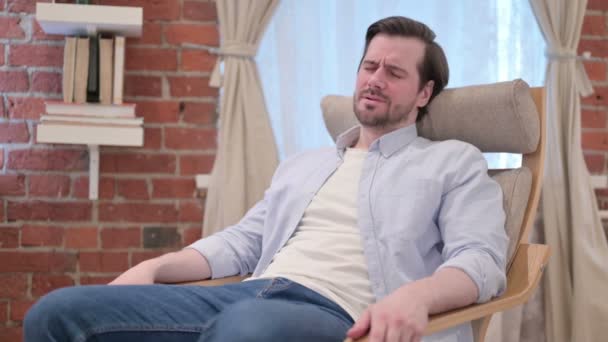 Hombre joven ocasional preocupado mientras está sentado en el sofá — Vídeos de Stock