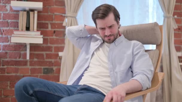 Unge man som har ont i nacken när han sitter på soffan — Stockvideo