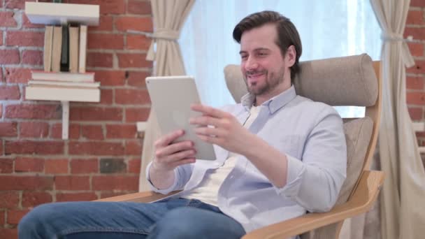 Случайный молодой человек разговаривает на видео-звонок на планшете на диване — стоковое видео