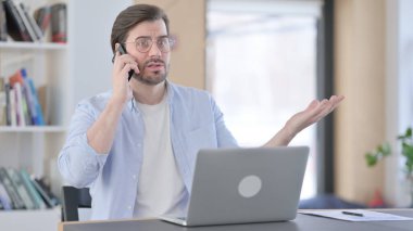 Dizüstü bilgisayarlı Kızgın Adam Akıllı Telefonla Konuşuyor 