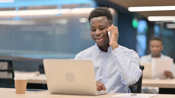 Afrikanischer Geschäftsmann mit Laptop im Smartphone-Gespräch — Stockfoto