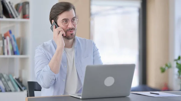Mann mit Brille und Laptop spricht auf Smartphone — Stockfoto