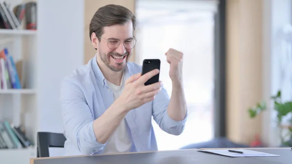 Hombre con gafas celebrando el éxito en el Smartphone en la oficina — Foto de Stock