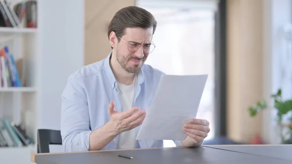 Hombre con gafas reaccionando a la pérdida mientras lee documentos —  Fotos de Stock