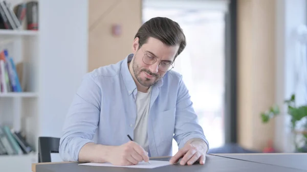 Pensiv man i glasögon skriver på papper, tänker — Stockfoto