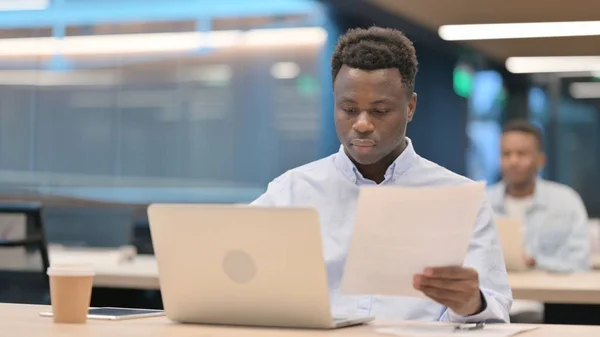 Homme d'affaires avec ordinateur portable lecture de documents dans le bureau — Photo