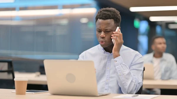 Wütender afrikanischer Geschäftsmann mit Laptop im Smartphone-Gespräch — Stockfoto