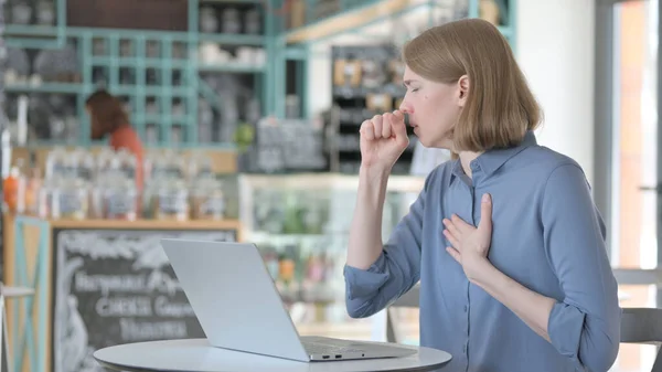 Young Woman Coughing while using Laptop in Cafe