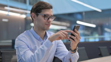 Genç adam iş yerinde akıllı telefon kullanıyor.