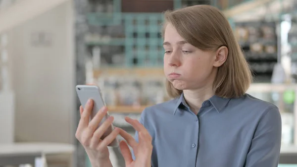 Porträt einer jungen Frau, die auf Verlust mit dem Smartphone reagiert — Stockfoto