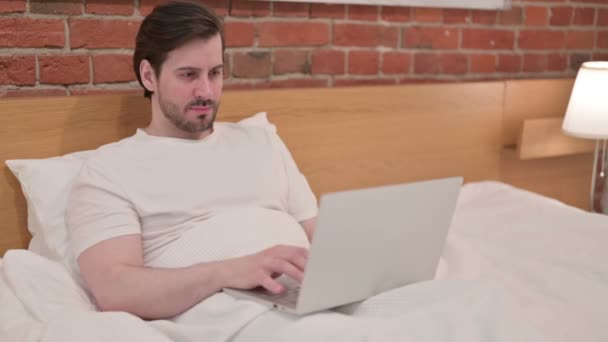어린 남자가 침대에서 노트북을 생각하며 일하다 — 비디오