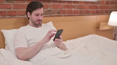 Genç İşadamı yatakta akıllı telefon kullanıyor.