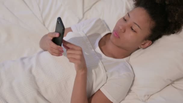 ベッドで寝ている間にスマートフォンを使うアフリカの女性 — ストック動画
