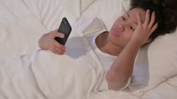 アフリカの女性はベッドでスマートフォンの損失に反応します — ストック動画