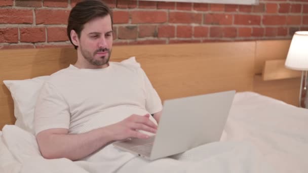 Casual giovane uomo con computer portatile avendo mal di testa a letto — Video Stock