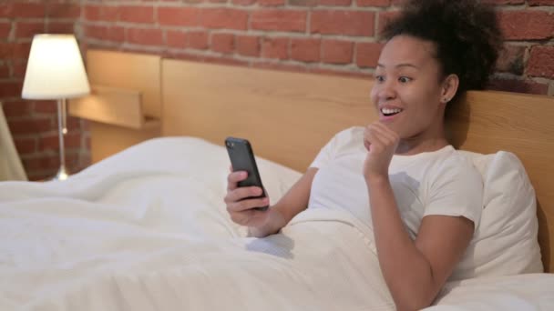 Mujer africana celebrando el éxito en el Smartphone en la cama — Vídeos de Stock