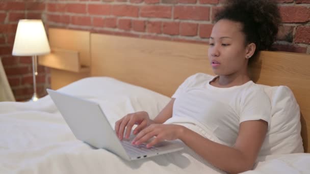 Mujer africana con dolor de cuello trabajando en el ordenador portátil en la cama — Vídeos de Stock