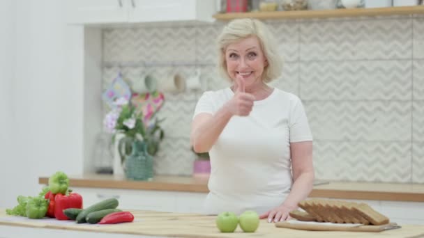 Senior gammal kvinna visar tummen upp när du står i köket — Stockvideo
