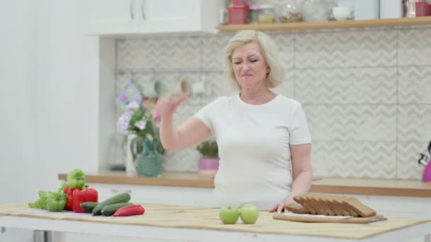 Idős öregasszony mutatja hüvelykujját le, miközben áll a konyhában — Stock videók