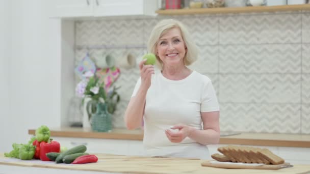 Gezond senior oude vrouw toont duimen omhoog terwijl het houden van Apple in de keuken — Stockvideo