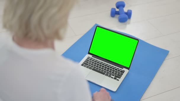 Vista trasera de la anciana mayor haciendo yoga mientras mira el ordenador portátil con pantalla clave de croma — Vídeo de stock
