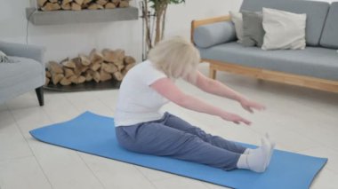 Yaşlı kadın evde yoga yaparken sırt ağrısı çekiyor.