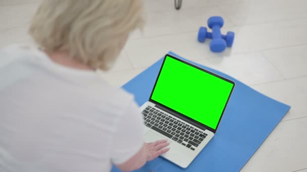 Vista trasera de la anciana mayor usando el ordenador portátil con la pantalla dominante del croma en la estera del yoga — Vídeo de stock