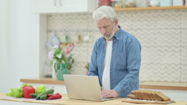 Привлекательная пожилая пара, работающая над ноутбуком на кухне — стоковое видео