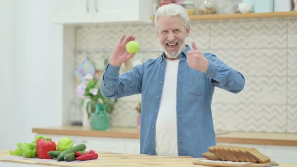 Gesunder Senior zeigt Daumen hoch, während er Apple in der Küche hält — Stockvideo