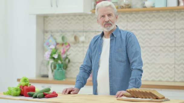 Gezonde oudere man glimlachend naar de camera terwijl hij in de keuken staat — Stockvideo