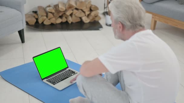 Anciano mayor usando el ordenador portátil con pantalla verde en la estera de yoga — Vídeo de stock