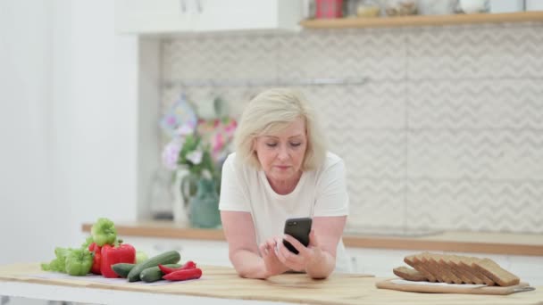 Atractiva anciana mayor usando Smartphone en la cocina — Vídeos de Stock